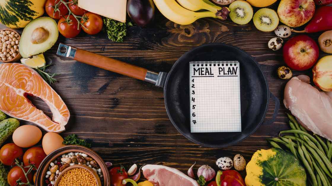 Healthy whole-food ingredients and a weekly meal plan notebook representing simple meal planning for weight loss